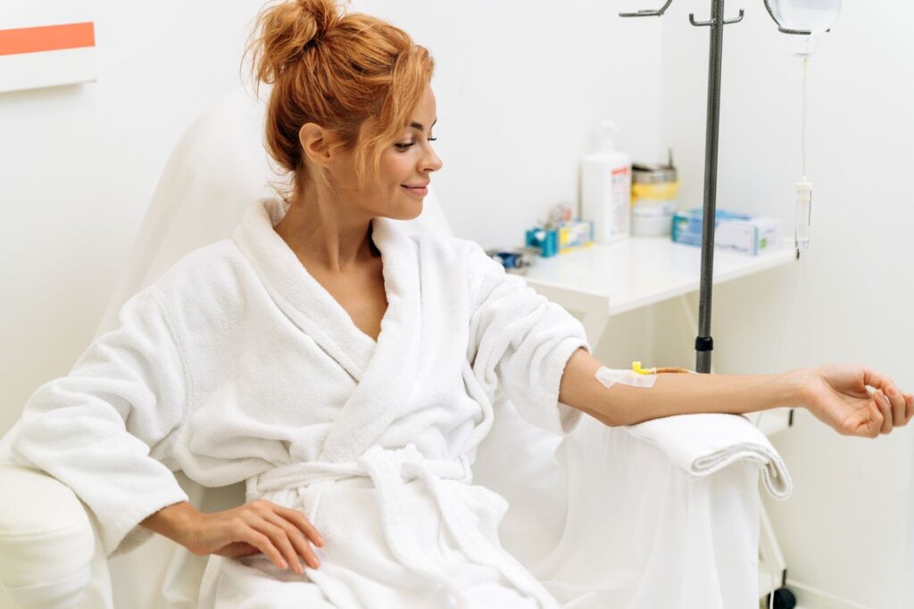 Woman in a white robe relaxing in a wellness chair while receiving an IV vitamin infusion