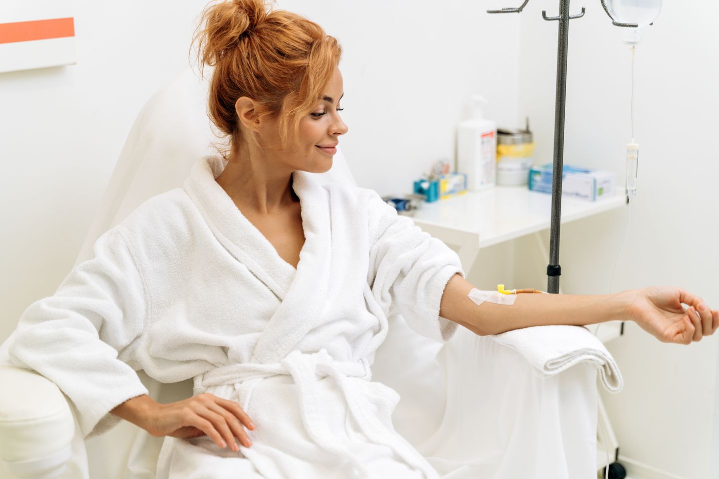 Woman in a white robe relaxing in a wellness chair while receiving an IV vitamin infusion