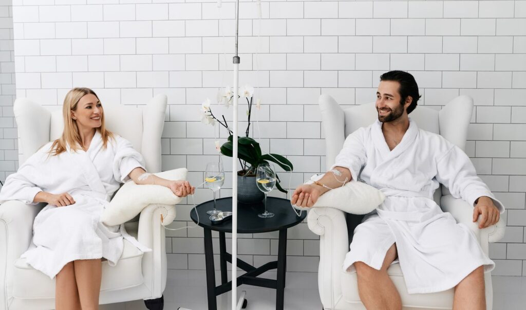 Woman receiving vitamin IV infusion therapy beside her partner in a modern wellness center