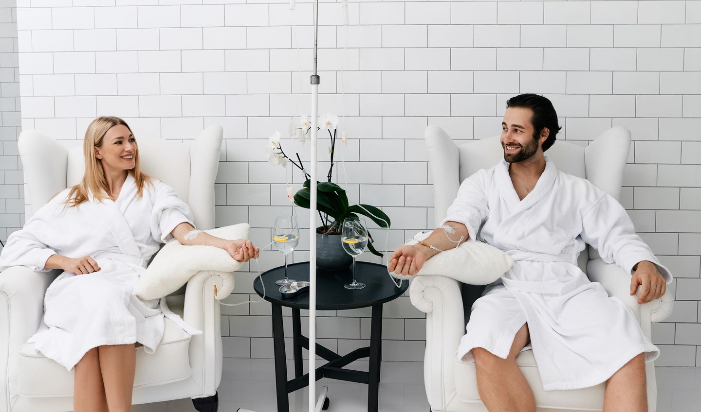 Woman receiving vitamin IV infusion therapy beside her partner in a modern wellness center